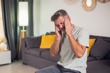 Closeup of man suffering from headache at home, touching his temples, copy space, blurred...