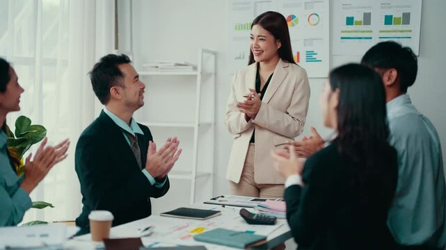 Celebrating success, a group of happy businesspeople claps hands together, congratulating a colleague on completing a successful project during a productive meeting