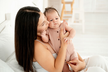 mom with a newborn baby, a young mother holds a small newborn baby in her arms, gently hugging and kissing him at home on the bed, happy motherhood