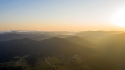 Mountains surrounded by forests in the colorful rays of the setting sun, in Bulgaria. Aerial shot with a drone