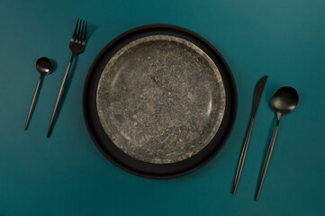 Top view of brown marble plate, black plate and cutlery on dark green background. Food...