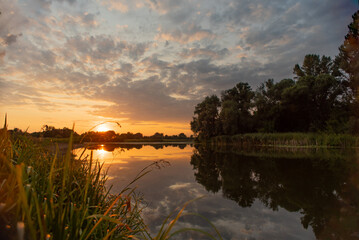 Obraz premium The sun sets over the horizon in front of a river. Evening landscape with bright colored sky