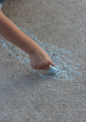 A child draws on the asphalt with crayons in summer