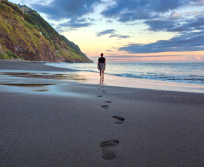 Silhouette of a young woman walking alone and leaving footprints on the sandy volcanic beach....