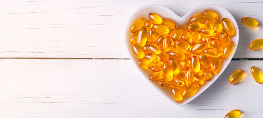 A heart-shaped white bowl filled with yellow fish oil soft capsules on a wooden table