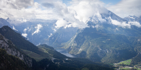 Day alpine landscape scenery with green valley, lake and snowy mountain peaks in clouds, Germany