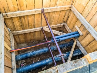 View into a wooden fenced excavation pit of a construction site with pipes and cables.