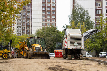 A machine cuts asphalt at a construction site near tall buildings