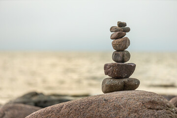 A neatly stacked pile of stones balances on a large rock, set against the backdrop of a calm sea at dusk. The tranquil scene embodies simplicity and harmony