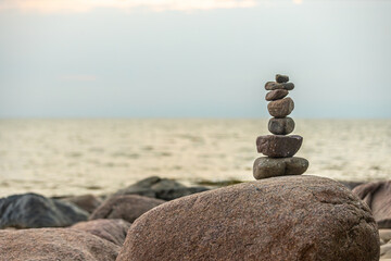 A neatly stacked pile of stones balances on a large rock, set against the backdrop of a calm sea at dusk. The tranquil scene embodies simplicity and harmony