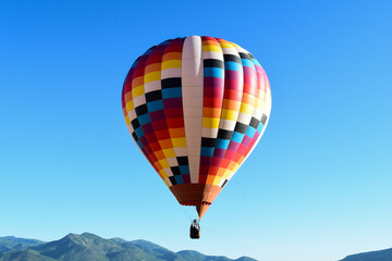 Fototapeta premium A colorful hot air balloon flying over the peaks of Utah on a bright blue sunny day