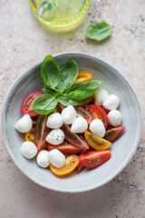 Grey plate with italian caprese salad on a beige granite background, vertical shot, high angle view