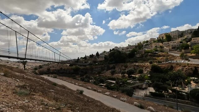the suspension bridge over Gei Ben Hinnom near the Old City of Jerusalem, with the Mount of Olives and cloudy skies in the background