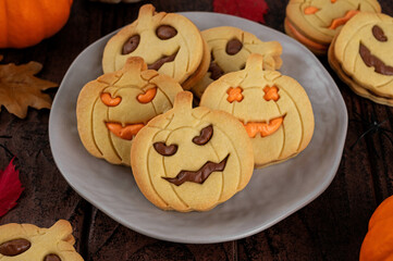 Halloween pumpkin shaped sandwich cookies with sweet cream filling on a dark wooden background. Jack o lantern cookies.