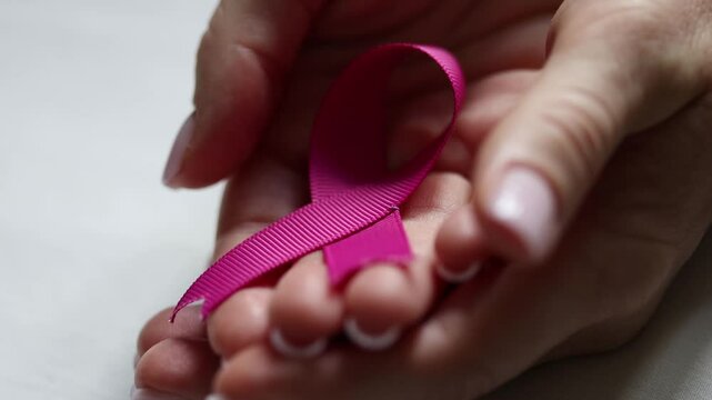Closeup of hands holding a pink ribbon