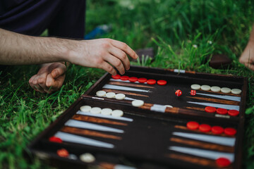 Hands playing backgammon on grass in a relaxed outdoor setting