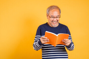 Portrait smiling Asian old man wearing glasses reading a book studio shot isolated yellow...