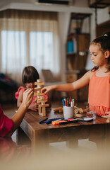 Two young girls engaged in a creative play activity with wooden blocks on a table at home, fostering teamwork and concentration.