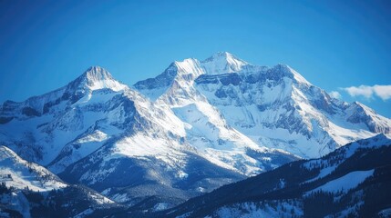 Obraz premium Snow-covered mountain peaks under a clear blue sky, with sunlight reflecting off the snow.