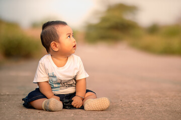 cute asian baby sitting on the road. baby boy facing sideways wearing white clothes. photo...