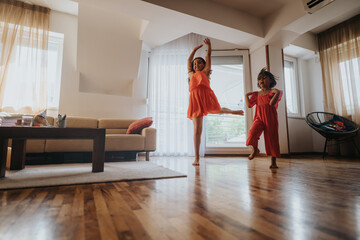Two kids in vibrant dresses energetically dance in a sunlit living room, expressing joy and...