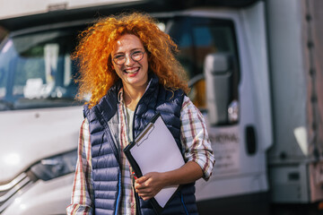 Ginger woman truck driver standing in front of her truck with a paper and write something....