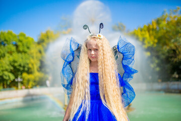 A little girl dressed as a fairy in front of a fountain. The concept of a magical holiday. Princess...