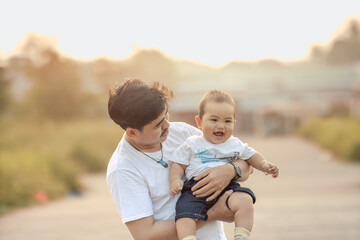 Fototapeta premium a father holding and looking at a baby boy with a warm smile. father and baby boy look happy and enjoy the afternoon atmosphere.