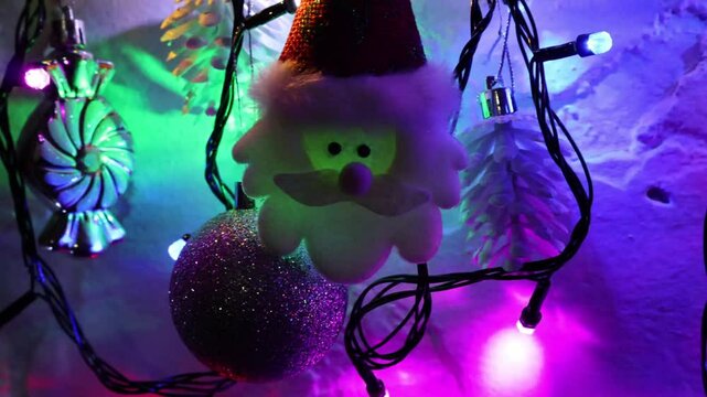 Una toma de cerca de una decoracion de navidad y fin de a&ntilde;o con una cara de santa claus  rodeado de varias luces con bombillos de varios colores en movimiento en la oscuridad