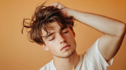 Obraz premium A young man running his fingers through his messy, tousled hairstyle, giving a relaxed, effortlessly stylish appearance.