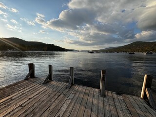 Scenic lake view from wooden dock with boats and mountains at sunset

