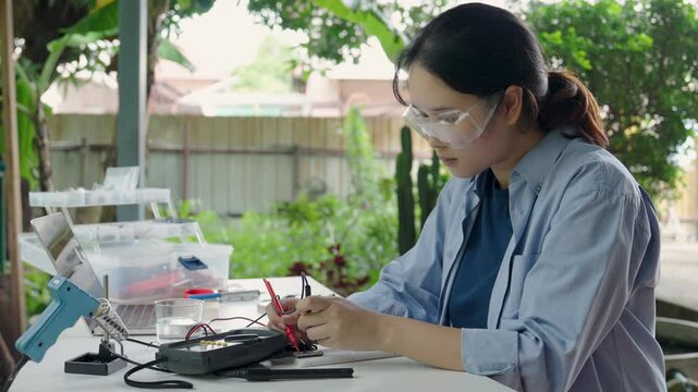Asian woman programming microcontroller to control analog dissolved oxygen sensor. Using electric meter to monitor microcontroller operation. Agriculture and aquaculture. Internet of Things (IoT)