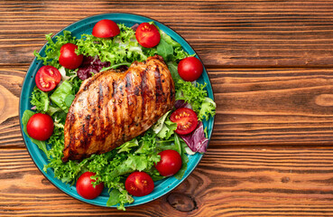 Grilled chicken breast ( fillet ) with lattuce salad and cherry tomatoes . Top view