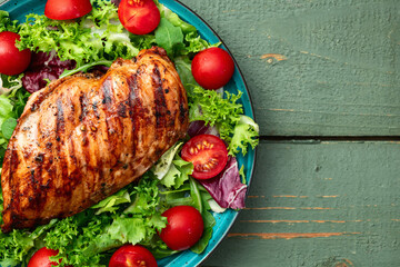 Grilled chicken breast ( fillet ) with lattuce salad and cherry tomatoes . Top view