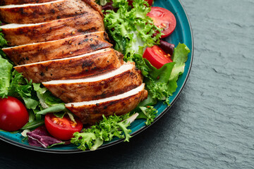 Grilled chicken breast ( fillet ) with lattuce salad and cherry tomatoes . Top view