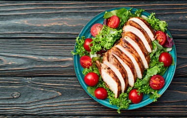 Grilled chicken breast ( fillet ) with lattuce salad and cherry tomatoes . Top view