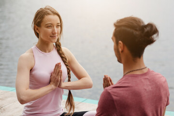 A couple engages in a yoga session by the lakeside at sunset. They perform a mindfulness exercise, demonstrating unity and tranquility while surrounded by nature.