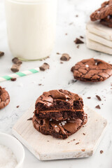 Brownie cookies stacked on a wooden coaster with scattered chocolate