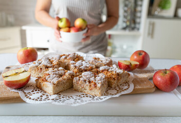 Homemade apple cake with crumbles and hazelnuts served by a woman with apron in the kitchen