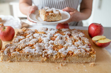 Homemade apple cake with crumbles and hazelnuts served by a woman with apron in the kitchen