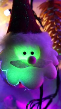Una toma de cerca de una decoracion de navidad y fin de a&ntilde;o con una cara de santa claus  rodeado de varias luces con bombillos de varios colores en movimiento en la oscuridad