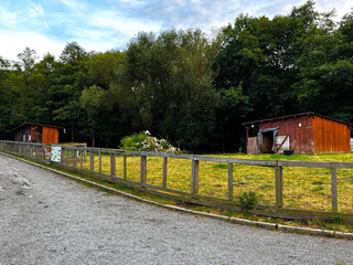 An old shabby orange barn behind a fence. The old barn is located on a green lawn.