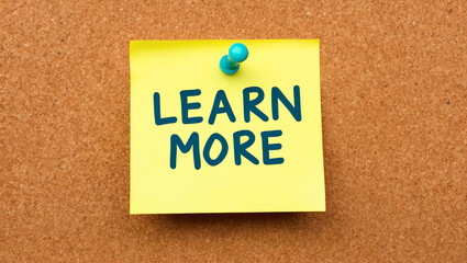 Learn More word written on a note sticky on corkboard