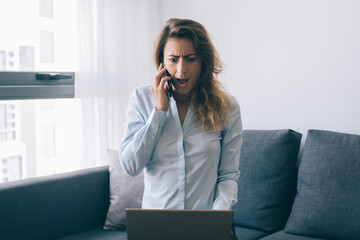 Amazed woman calling on phone and watching laptop