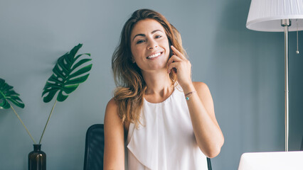 Enthusiastic female sitting at table talking on mobile and worki