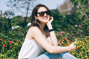 Young Asian lady in sunglasses with smartphone smiling and looking at camera