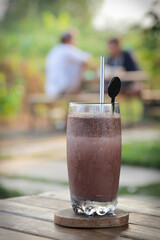 Iced chocolate drink served in clear glass on rustic wooden table. Beverage concept
