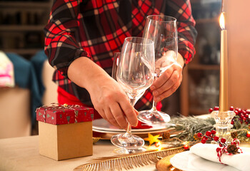 Close-up of hands placing wine glasses on a festive dinner table with Christmas decorations