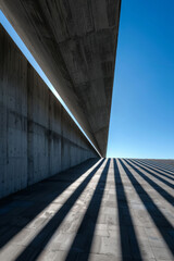 image showcases striking architectural composition with sharp lines and shadows, emphasizing interplay of light and structure. concrete surfaces create modern aesthetic against clear blue sky