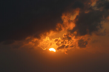 A fiery sunset partially obscured by dark clouds, casting a dramatic golden glow across the sky. Perfect for nature and weather-themed projects, creating a moody and atmospheric visual experience.